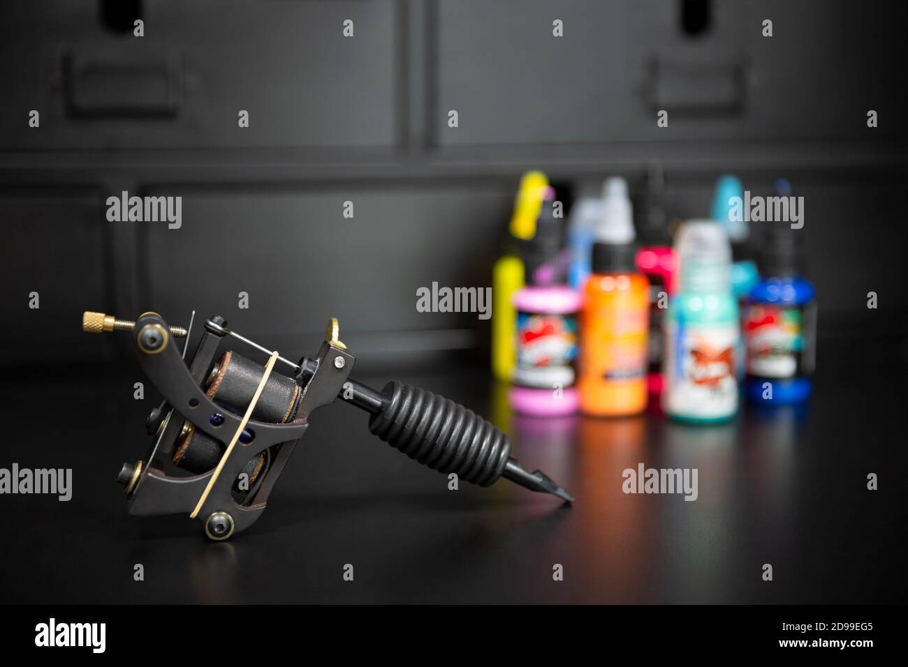 Primo piano della macchina per tatuaggio con bottiglie di inchiostro colorate su sfondo scuro. Set studio tatuaggio. Spazio per il testo. Foto Stock