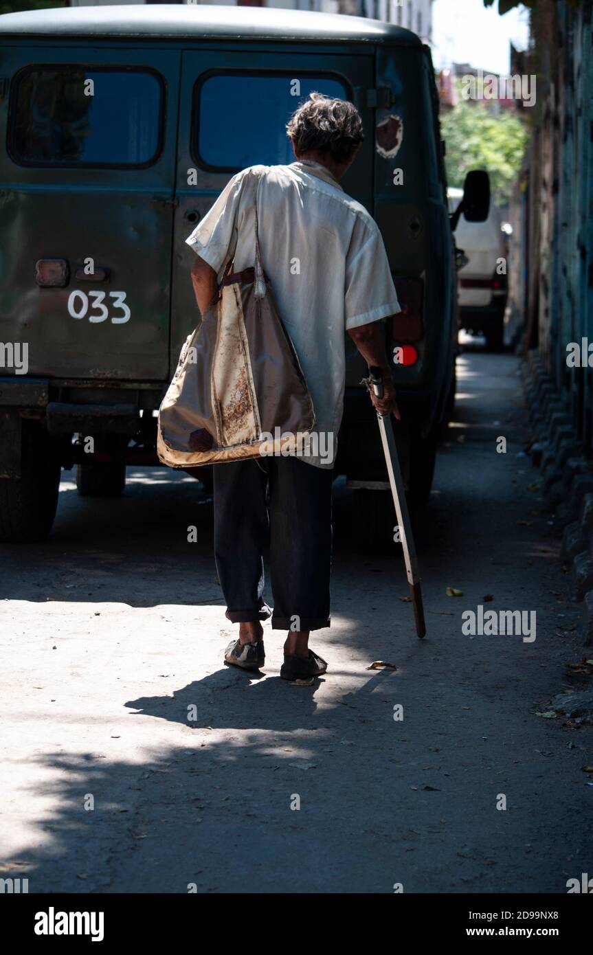 Vista posteriore del vecchio senza casa che cammina con un crutch e la sua borsa sporca Foto Stock