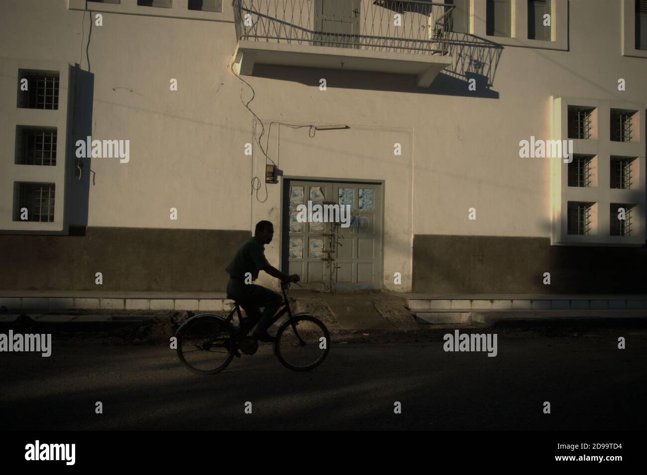Un ciclista pedalando su una strada, con un edificio in vecchio stile architettonico sta accentuando l'area del patrimonio culturale a Sibolga, Sumatra Nord, Indo Foto Stock
