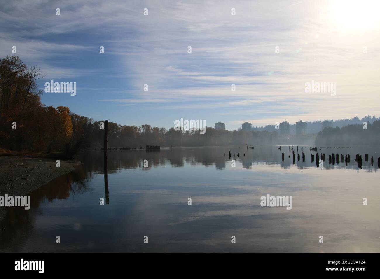 Una vista di alcuni grattacieli in lontananza con un corpo d'acqua calmo in primo piano. Ci sono palchi derelict sulla destra tutti sotto un clo blu Foto Stock