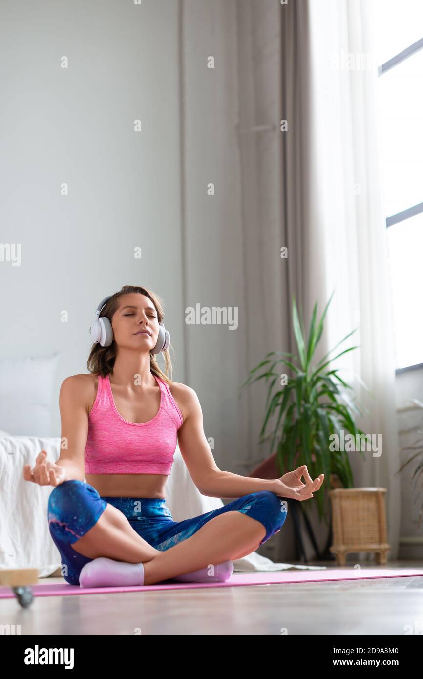 Yoga a casa. Foto verticale - ritratto a tutta lunghezza di una donna con occhi chiusi in posizione lotus. Foto Stock