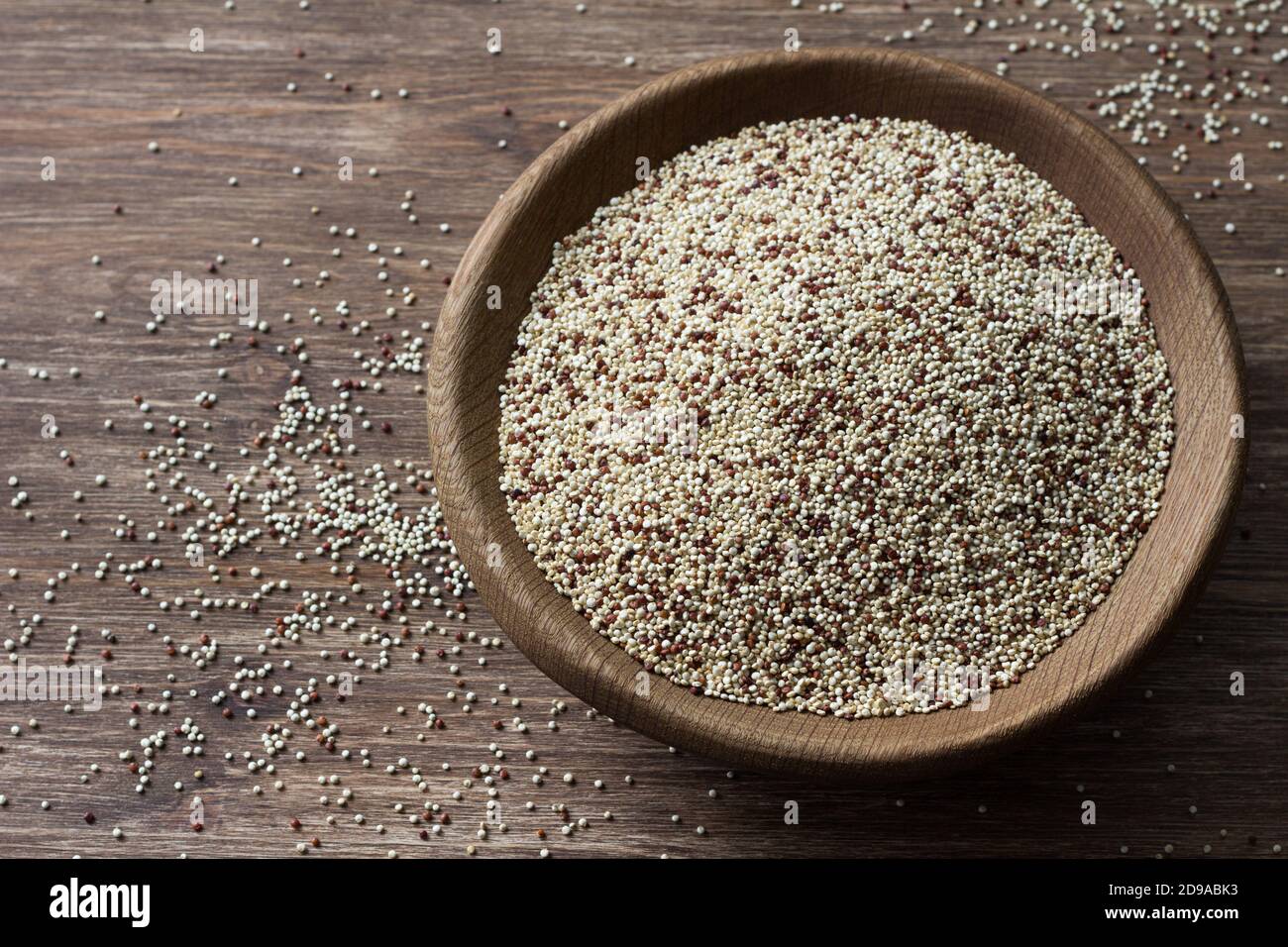 Quinoa crude mescolate in ciotola di legno su tavola di legno. Supercibo sano e senza glutine Foto Stock
