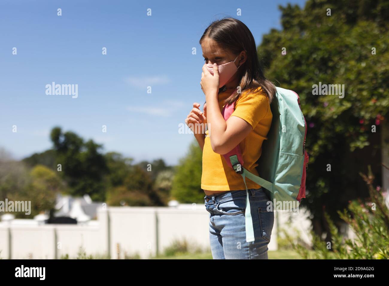 Caucasica ragazza con capelli scuri indossare maschera a piedi borsa scolastica per il trasporto Foto Stock