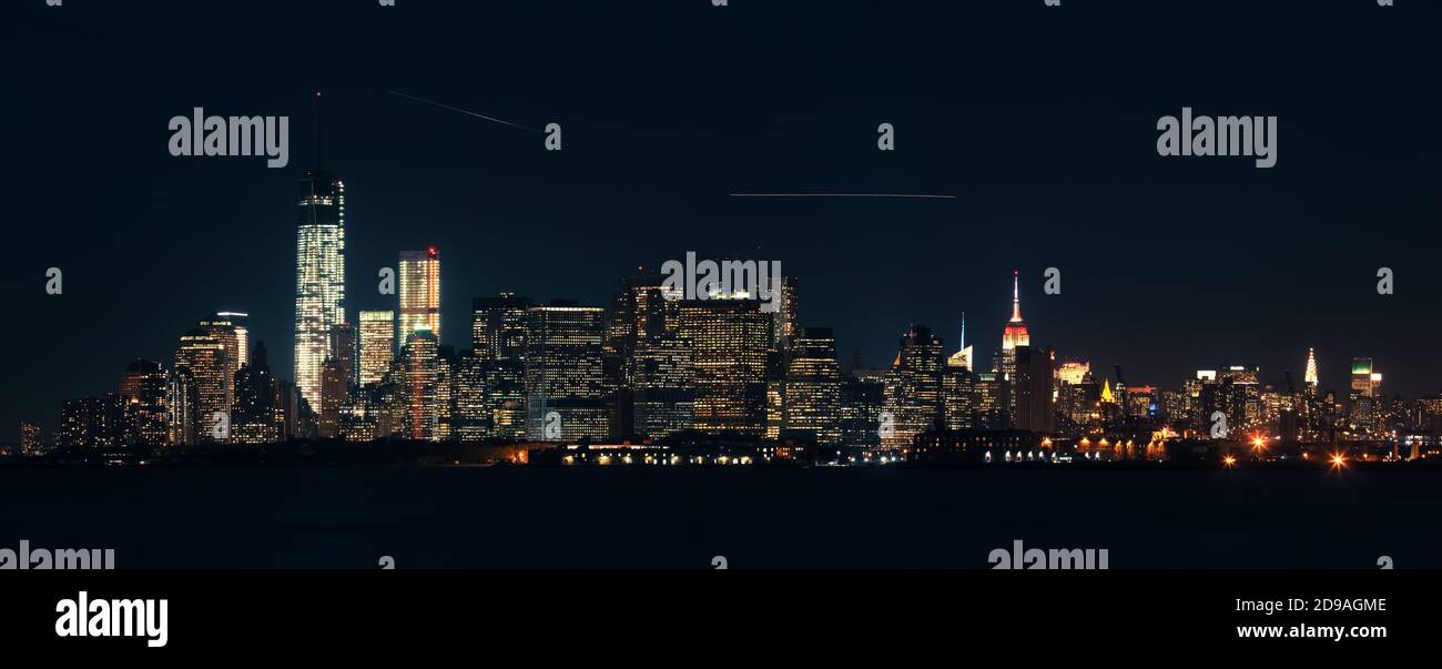 Panorama di Manhattan di notte. Finestre luminose di uffici e tracce di aeroplani nel cielo. Stati Uniti, New York Foto Stock