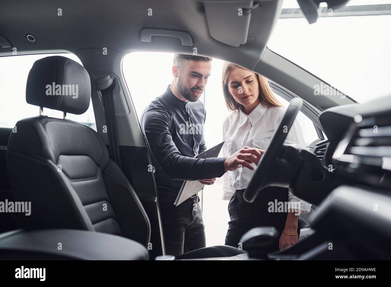 Donna che sceglie l'auto con l'aiuto di un assistente maschile all'interno il salone Foto Stock