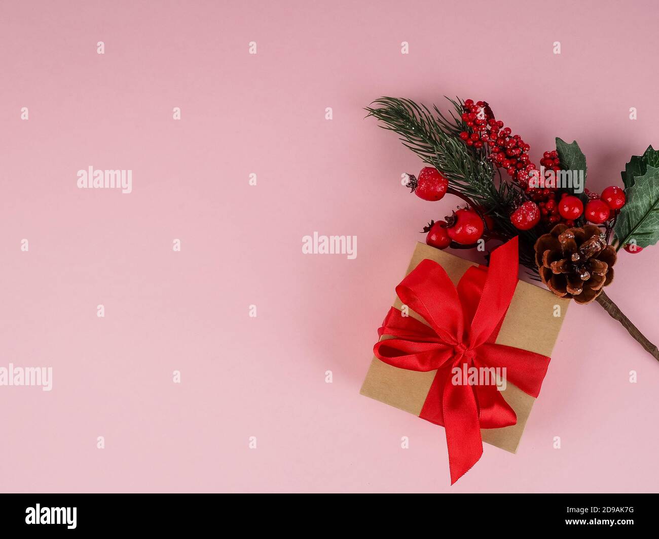 Confezione regalo con un nastro rosso su sfondo rosa, accanto a un ramo natalizio. Foto Stock