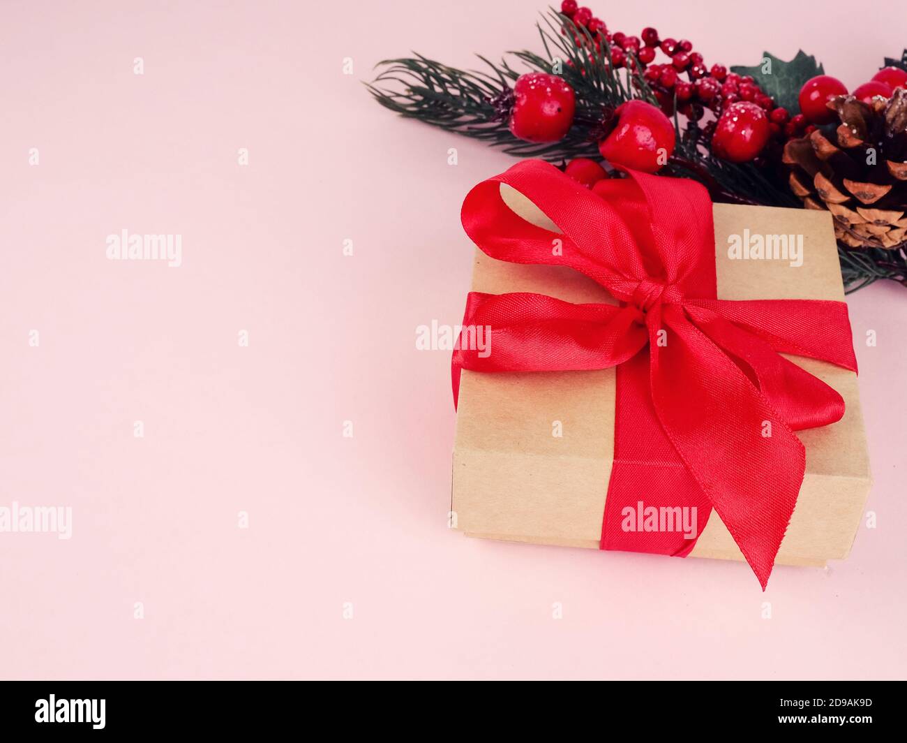 Confezione regalo con un nastro rosso su sfondo rosa, accanto a un ramo natalizio. Foto Stock