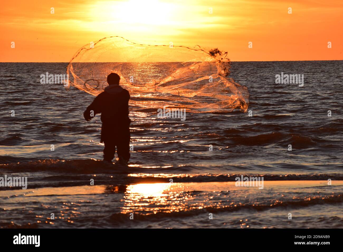 Pescatore che getta la sua rete nella luce del tramonto nel Mar Tirreno vicino a Roma. Immagini brillanti e sorprendenti con l'uomo in retroilluminazione e una rete perfetta. Foto Stock