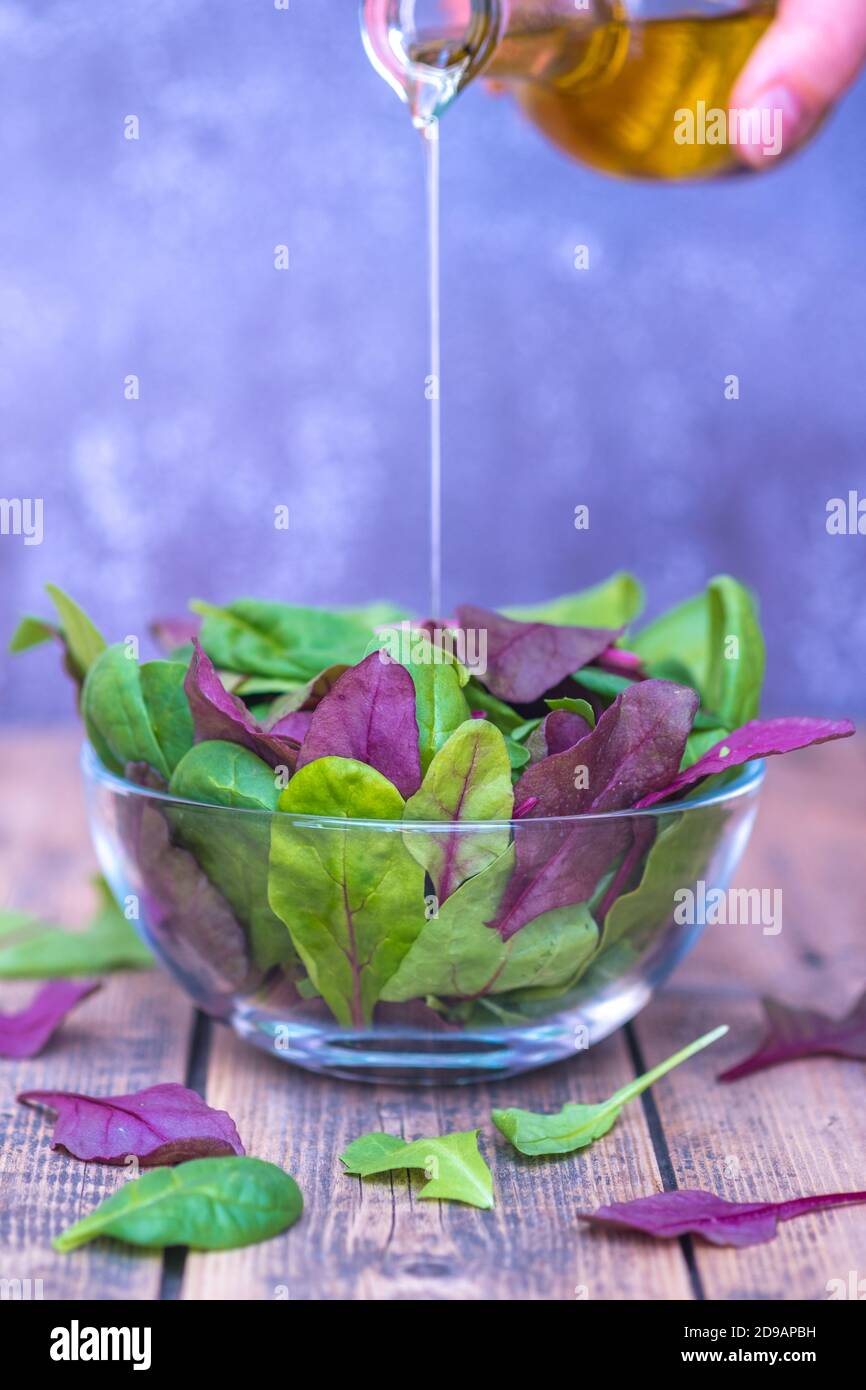 Foglie di insalata miste in una ciotola di vetro su sfondo di legno. Foto Stock