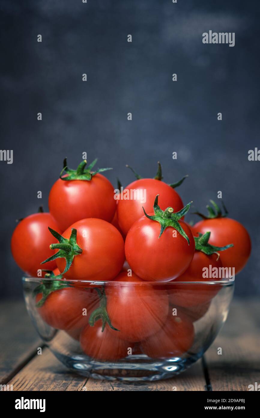 Pomodori ciliegini freschi in una ciotola di vetro su un legno sfondo Foto Stock