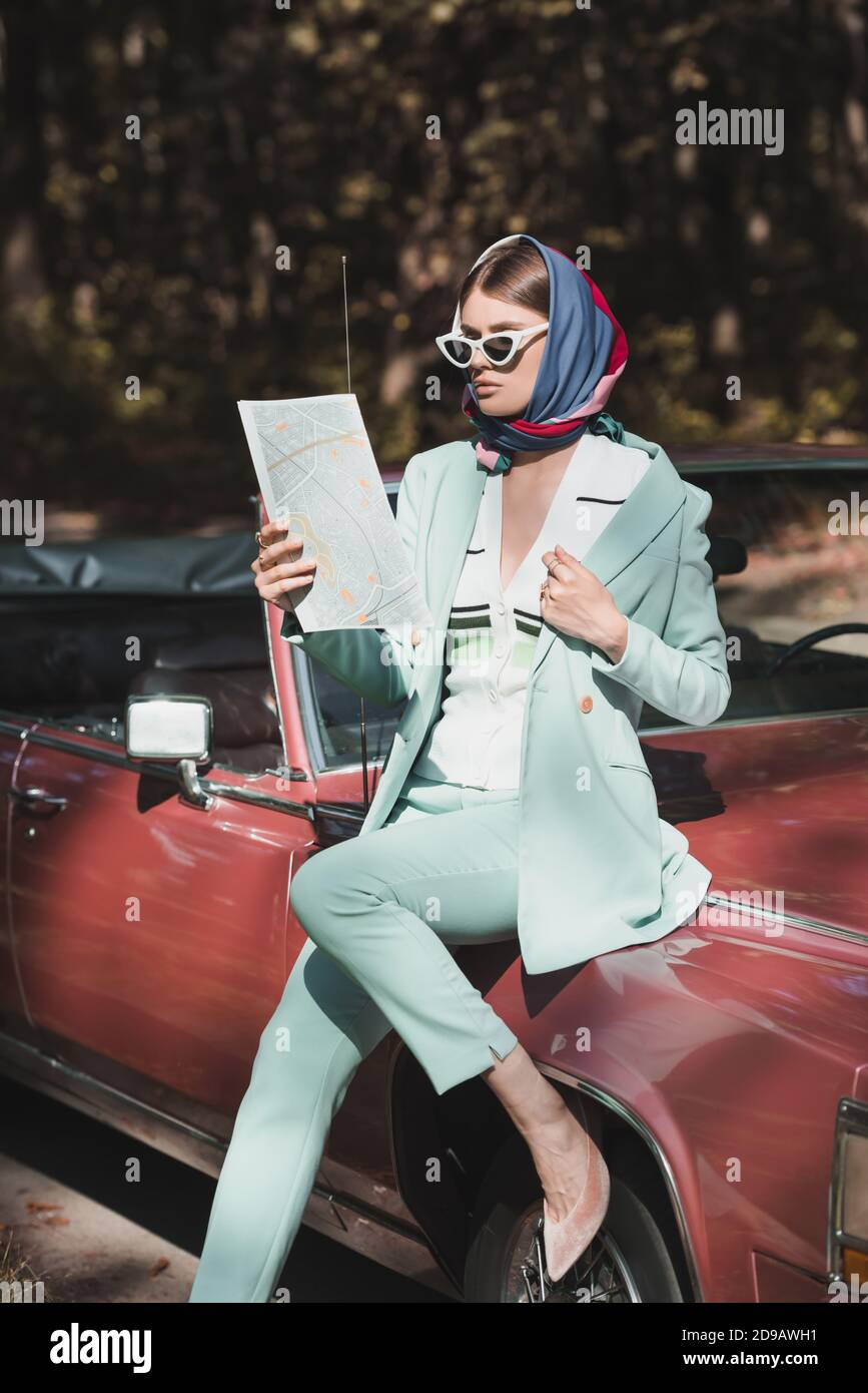 Donna elegante con occhiali da sole e foulard che tiene la mappa mentre si  siede sul paraurti dell'auto Foto stock - Alamy