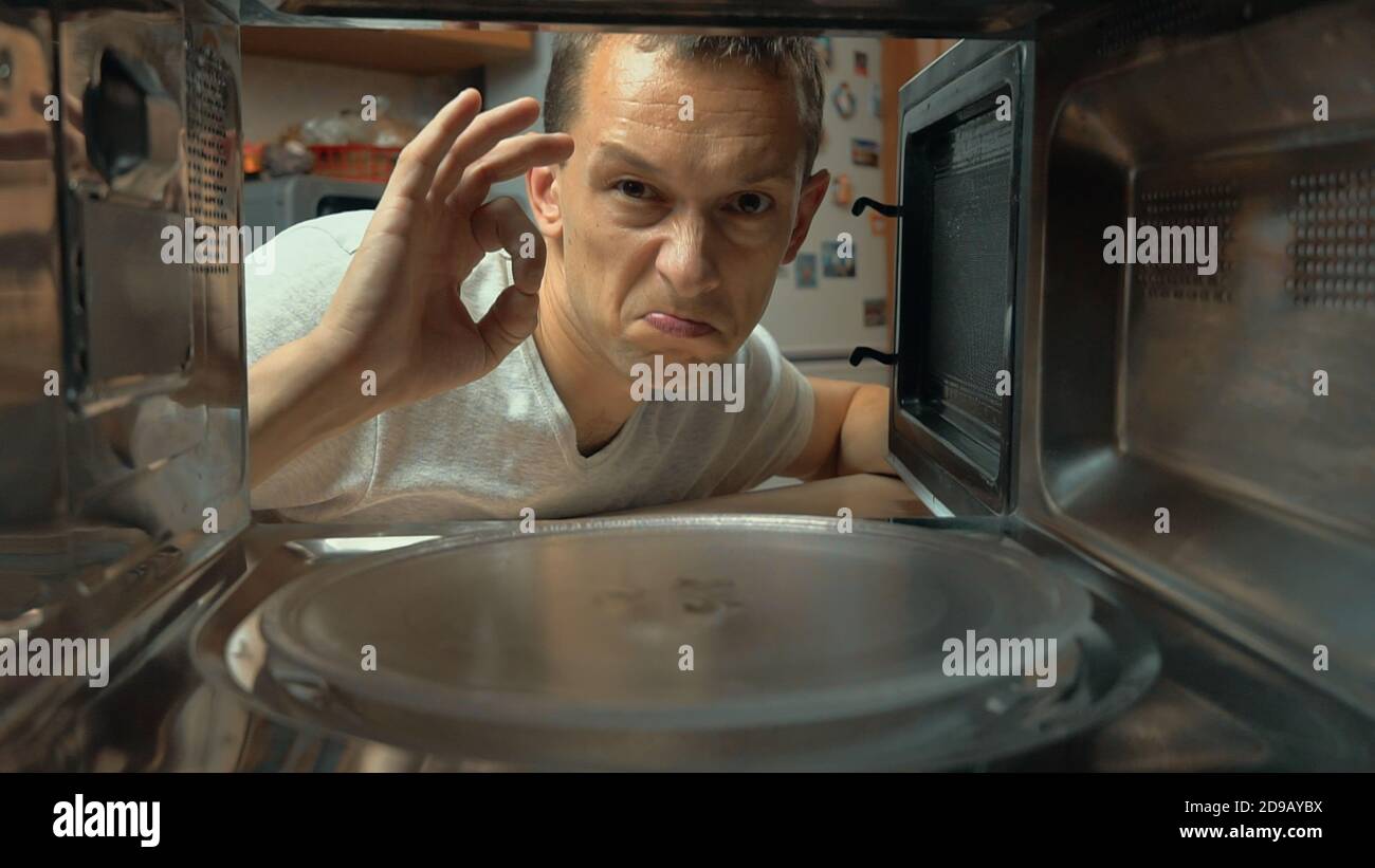 L'uomo apre il forno a microonde, guarda all'interno e mostra il segno OK.  Indica la qualità del lavoro o della cottura. Riprese dall'interno Foto  stock - Alamy