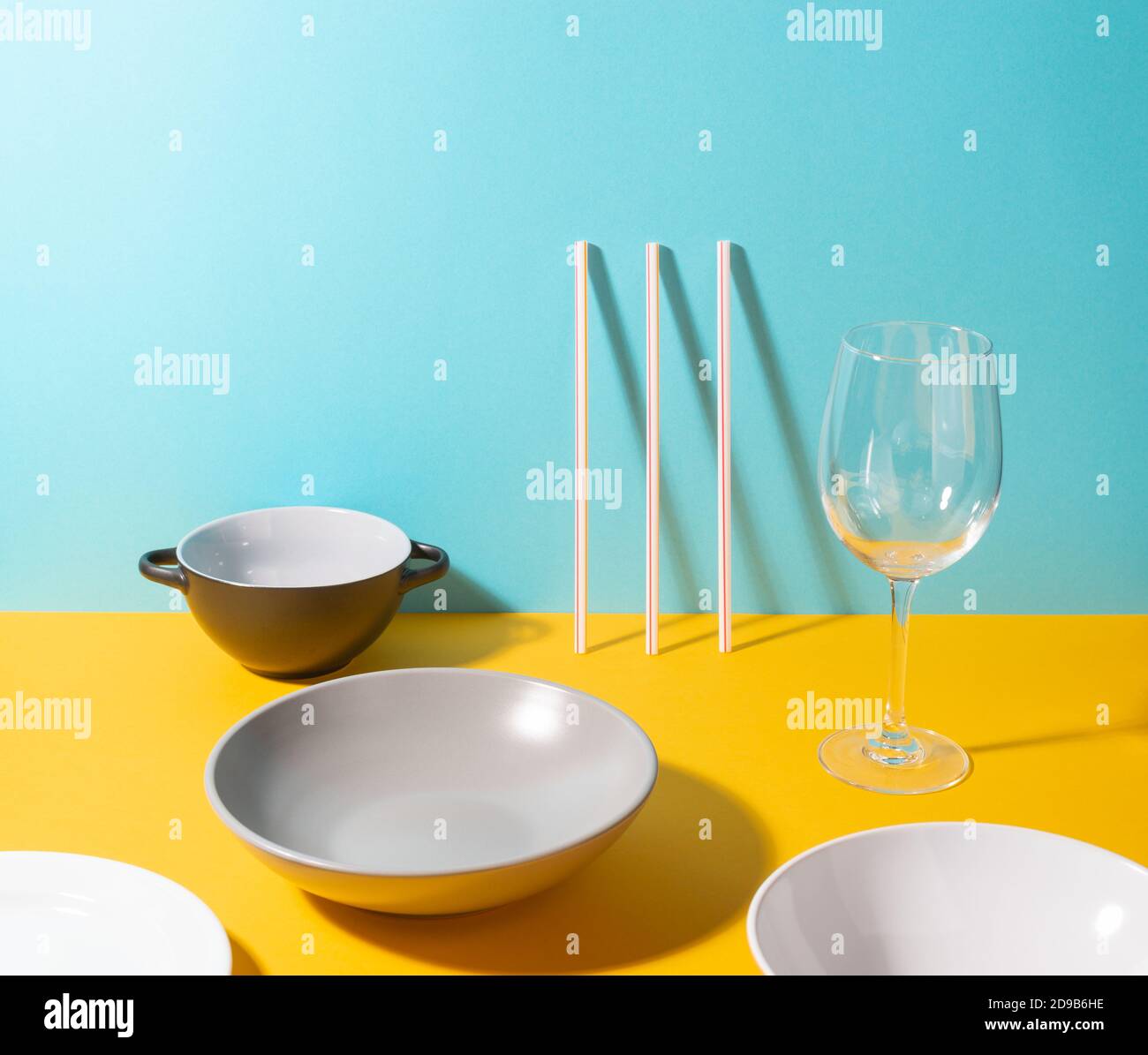 Vari piatti, cannucce e un bicchiere su sfondo giallo e blu Foto Stock