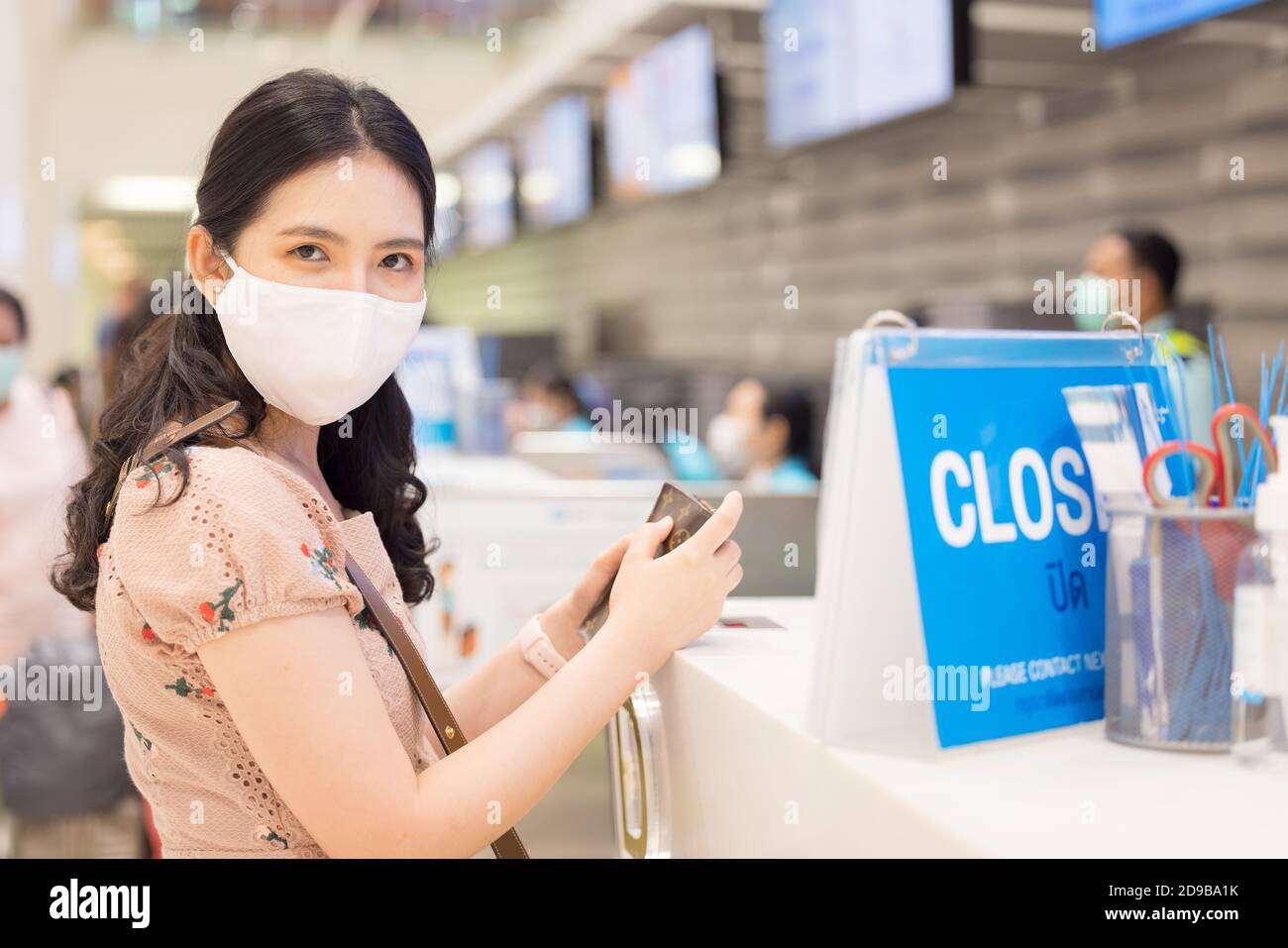 Donna asiatica con maschera igienica in piedi di fronte al banco cassa in aeroporto. Autoprotezione durante l'epidemia di COVID-19 o di coronavirus da parte di usi Foto Stock