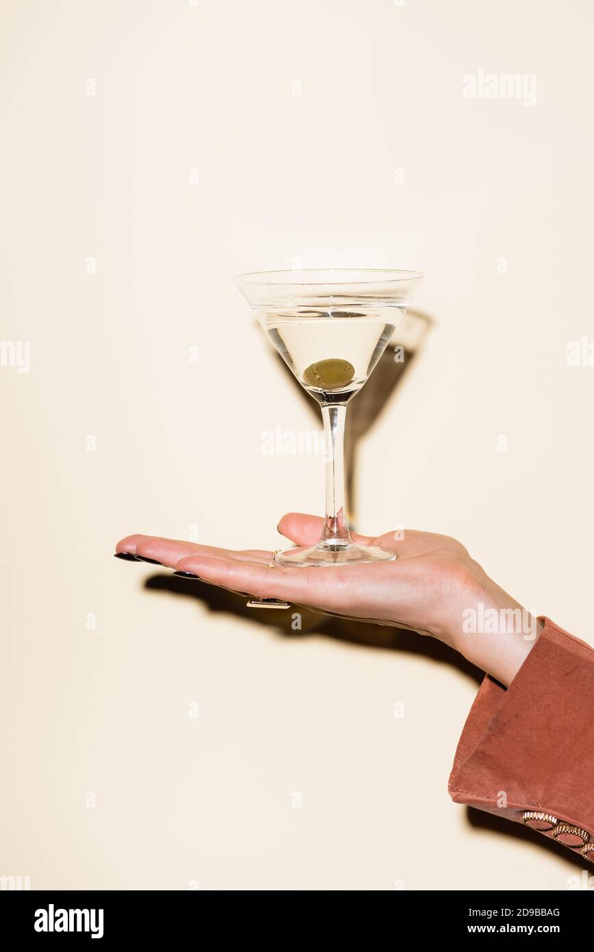 vista tagliata di donna che tiene vetro di martini con verde oliva in mano su bianco Foto Stock