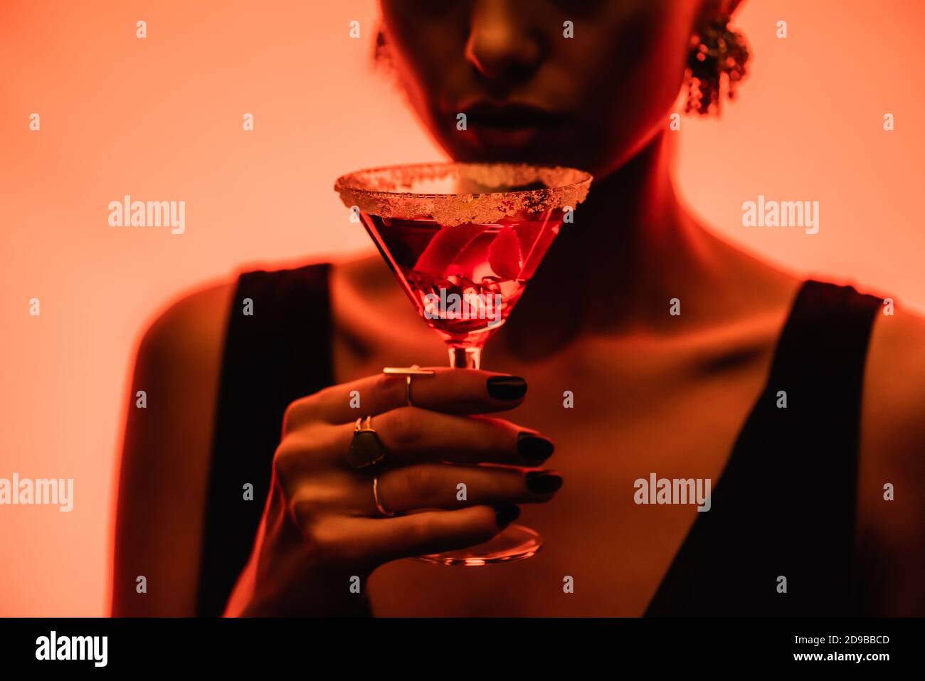 cocktail margarita con cubetti di ghiaccio e sale in mano donna su sfondo arancione sfocato Foto Stock