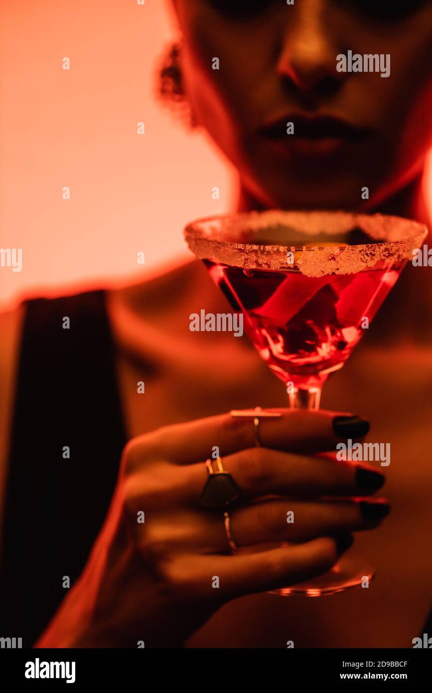 cocktail margarita con sale su bicchiere in mano alla donna su sfondo arancione sfocato Foto Stock