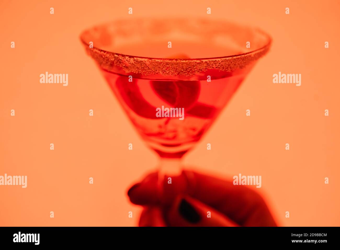 primo piano del cocktail margarita con cubetti di ghiaccio e sale in mano femminile su arancione Foto Stock