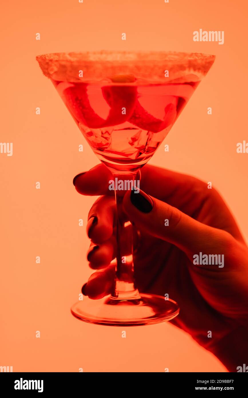 primo piano del cocktail margarita con cubetti di ghiaccio in femmina mano su arancione Foto Stock