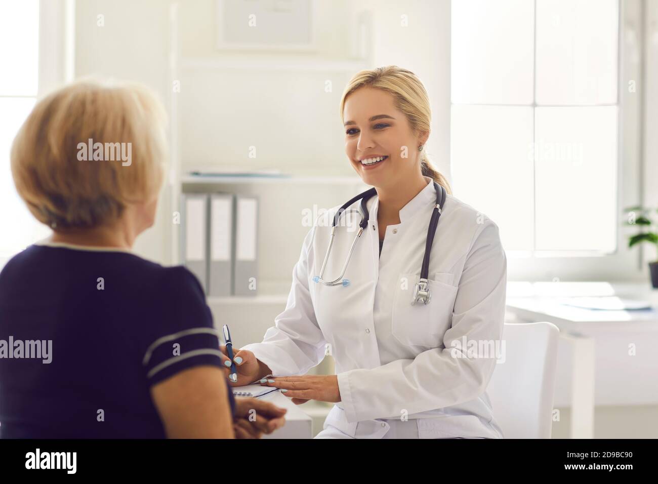 Donna medico seduta e prendere appunti durante la consultazione con maturo paziente donna Foto Stock