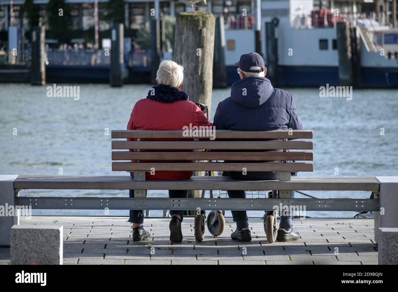 Coppia più anziana da dietro seduta su una panchina direttamente sul lungomare sulla banchina e godendo la vita portuale sotto il sole, fuoco selezionato Foto Stock