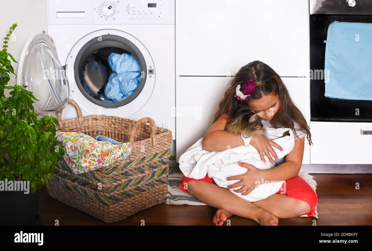La bambina bella si lava e gioca con il gattino B, lo asciuga con un asciugamano dopo il lavaggio. Il bambino si siede sul pavimento vicino alla lavatrice. Banner. Formato lungo. Foto di alta qualità Foto Stock