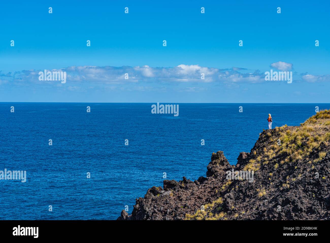 Donna in piedi su una cima di una scogliera e godendo la vista sull'oceano a Sao Miguel, Azzorre, bellissimo cielo blu Foto Stock