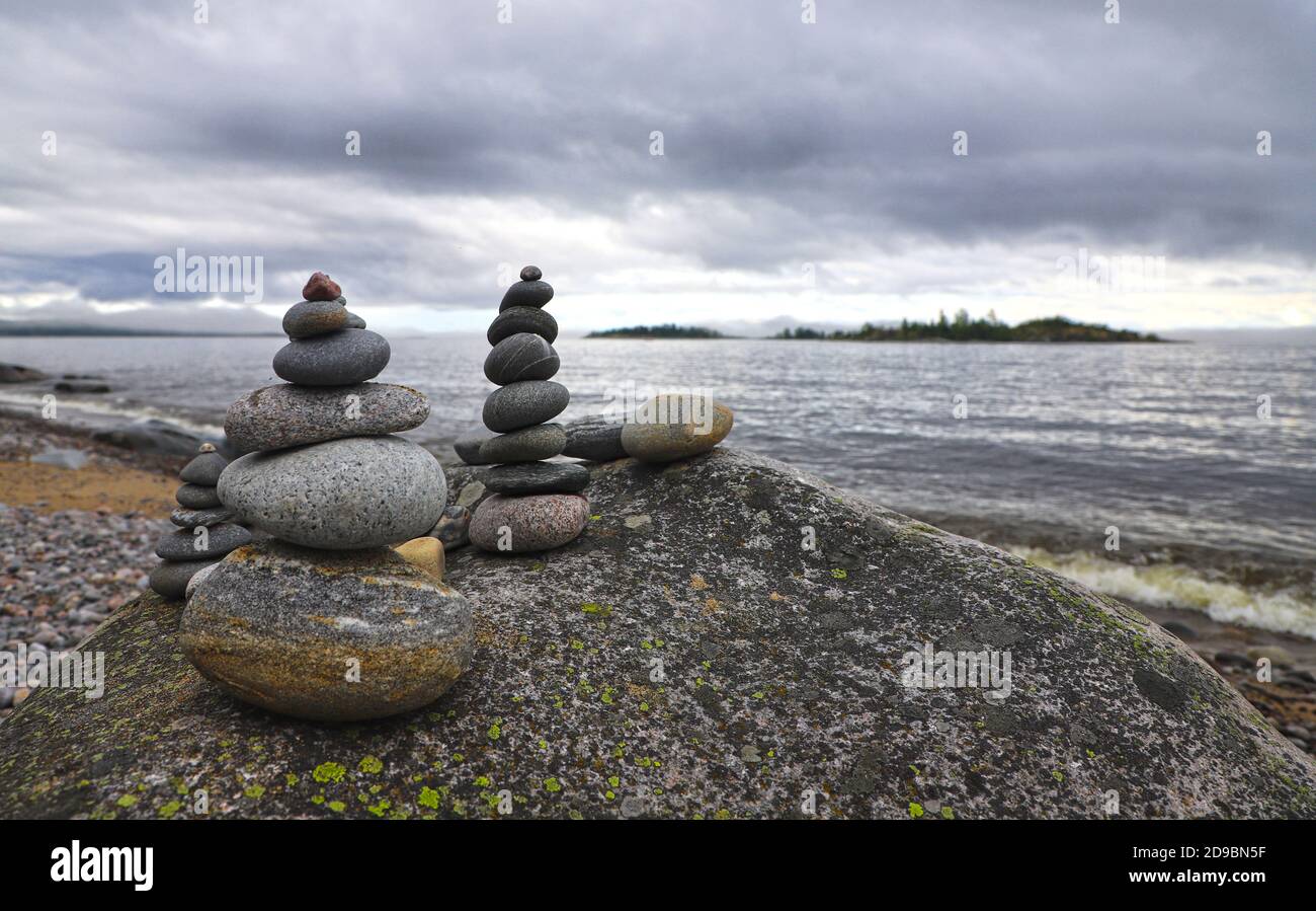 Zen torwr di ciottoli su una roccia, acqua ondulata os un lago e cielo nuvoloso sullo sfondo. Foto Stock