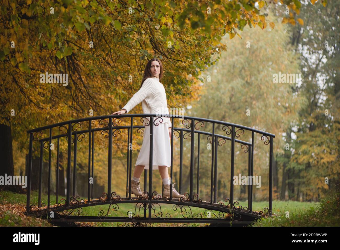 Giovane bella donna in hite accogliente maglione sul ponte al parco naturale in autunno giorno. Foto Stock