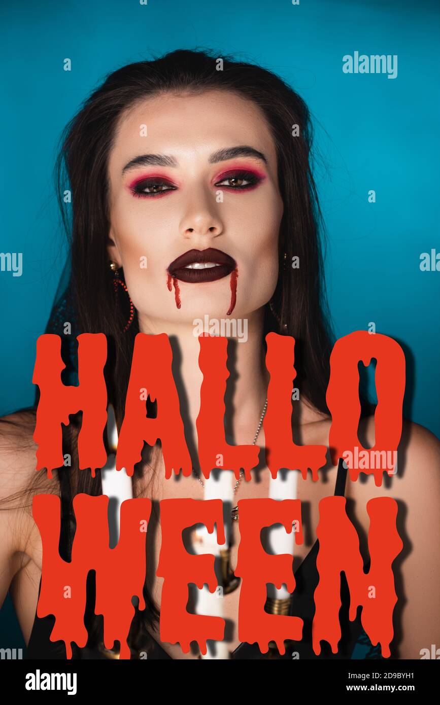 donna con sangue rosso sul viso vicino a candele brucianti e. scritta halloween blu Foto Stock