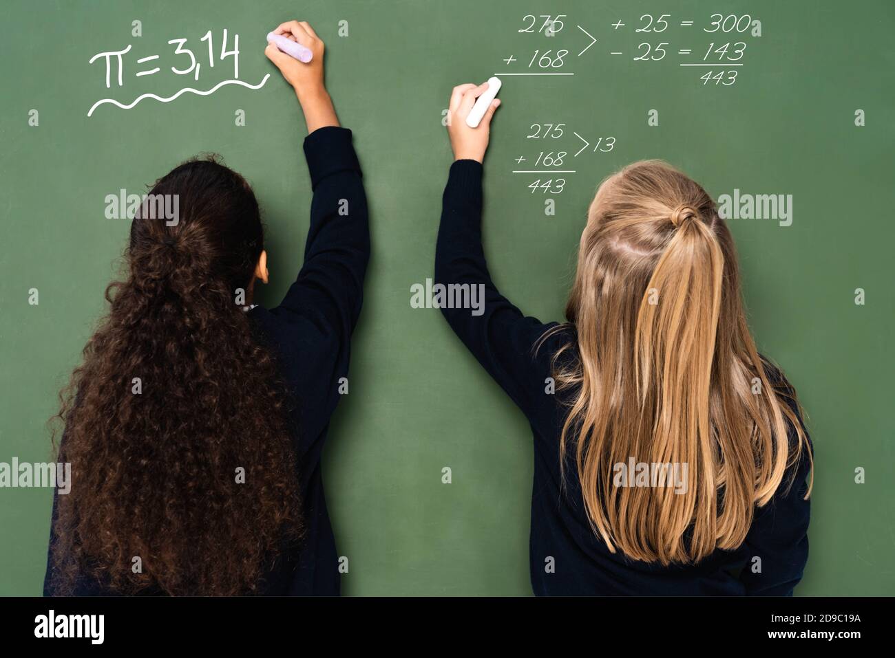 vista posteriore delle studentesse multiculturali che scrivono equazioni matematiche sulla lavagna Foto Stock