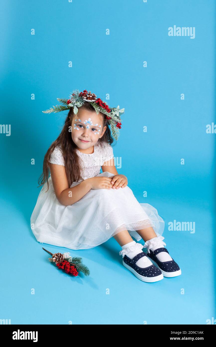 un bambino in un vestito bianco fiocco di neve e il trucco dei petali di  neve si siede sul pavimento in scarpe blu, isolate su uno sfondo azzurro  Foto stock - Alamy