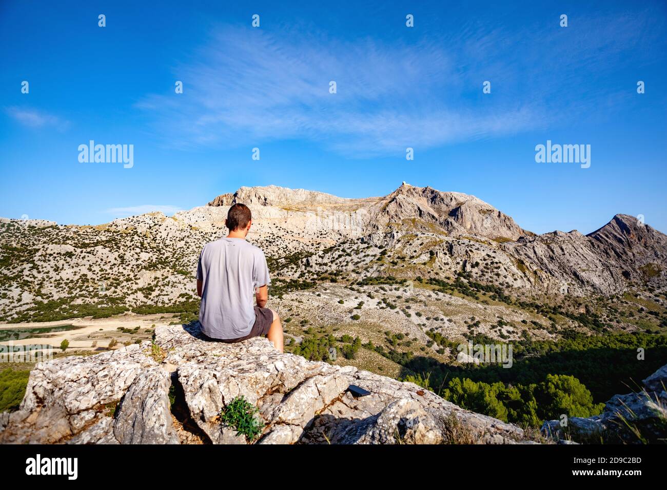 Giovane uomo di viaggio seduto sulla roccia nelle montagne di Maiorca Serra de Tramuntana e guardando al monte maggiore Puig, posto per il testo Foto Stock