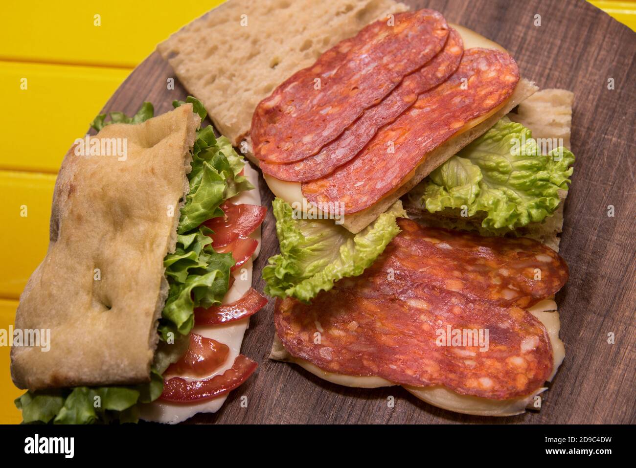 Soppressata di Calabria, salame tipico italiano con peperoncino, su un panino con lattuga e pomodoro su una superficie di legno Foto Stock