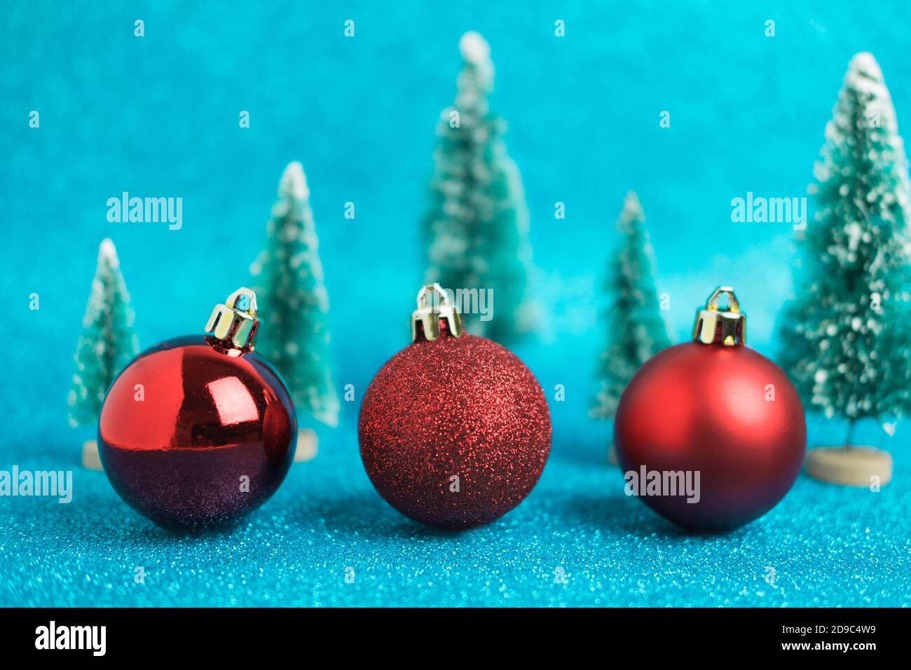 Natale sfondo festivo con tre palline di natale rosso, alberi giocattolo. Abstract glitter sfondo sfocato blu lucido ai aqua. Luminoso e scintillante wallp Foto Stock