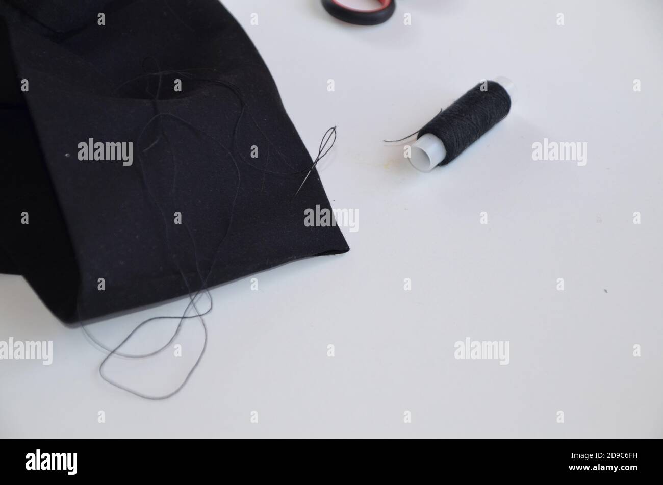 cucire ragazza con filo e ago in materiale nero. pantaloni a canapa. torce il filo in un ago. Uomo su misura che lavora nel suo negozio su misura, sartoria Foto Stock