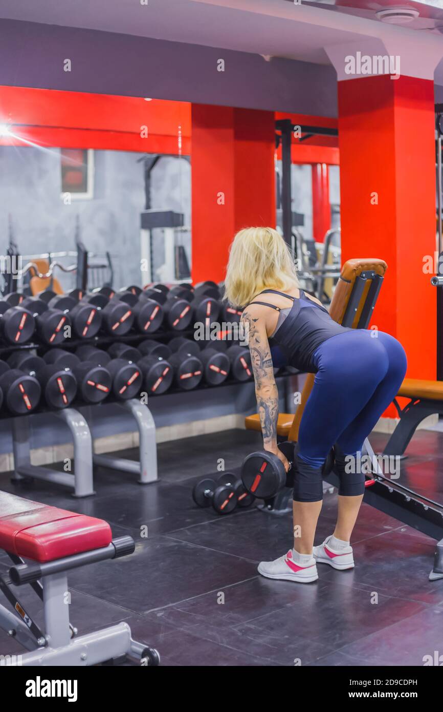 Atletica giovane donna bionda sollevamento manubri in palestra, fitness club. Salute, bodybuilding, formazione, benessere, stile di vita, sport e concetto di allenamento Foto Stock