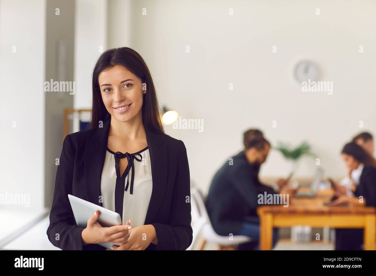 Felice giovane presidente di azienda femminile con tablet in mano in piedi in ufficio guardando la fotocamera Foto Stock