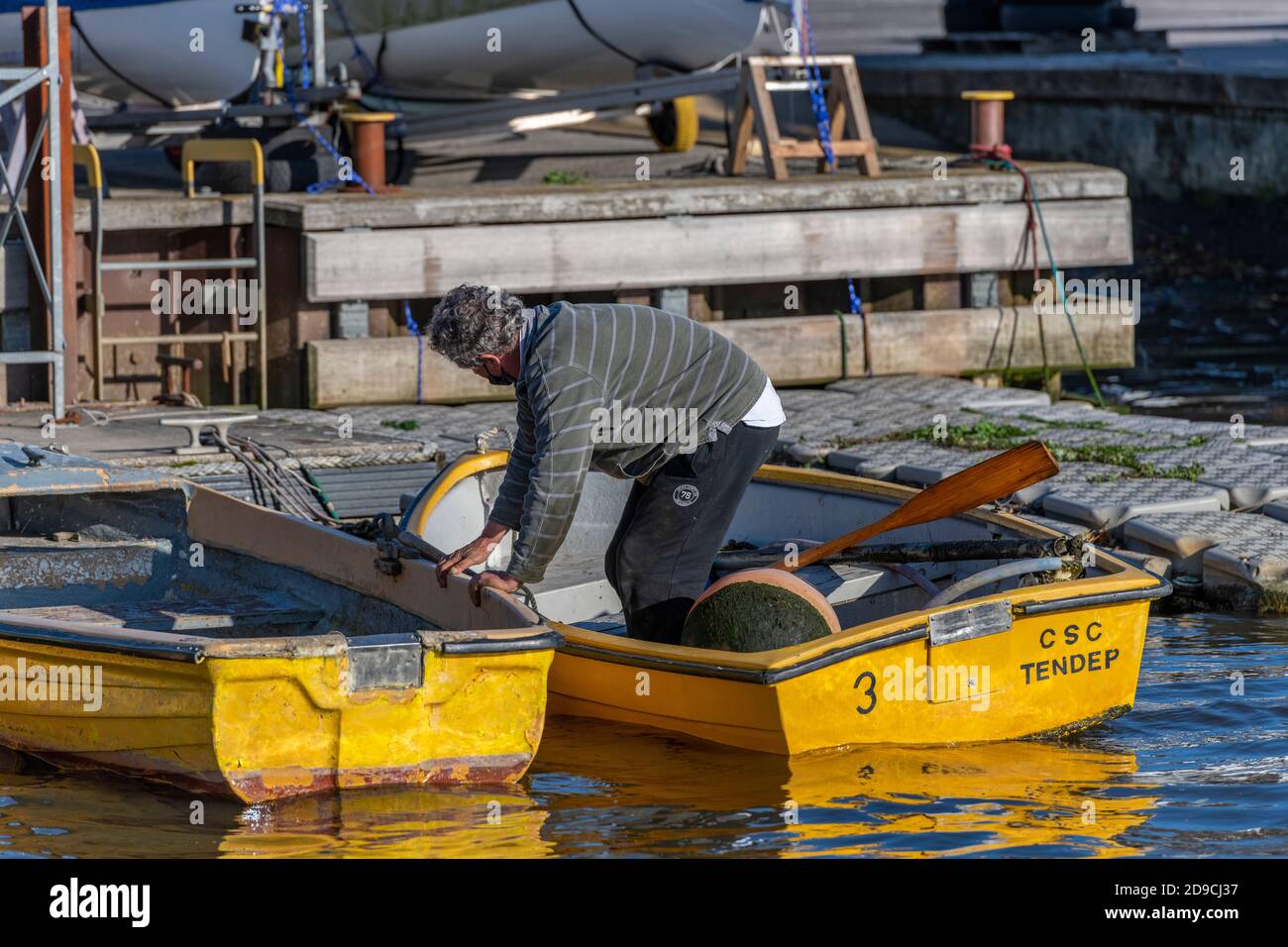 un uomo che sale da una piccola barca gialla a remi dopo aver ormeggiato accanto ad altre barche in un porticciolo. Foto Stock