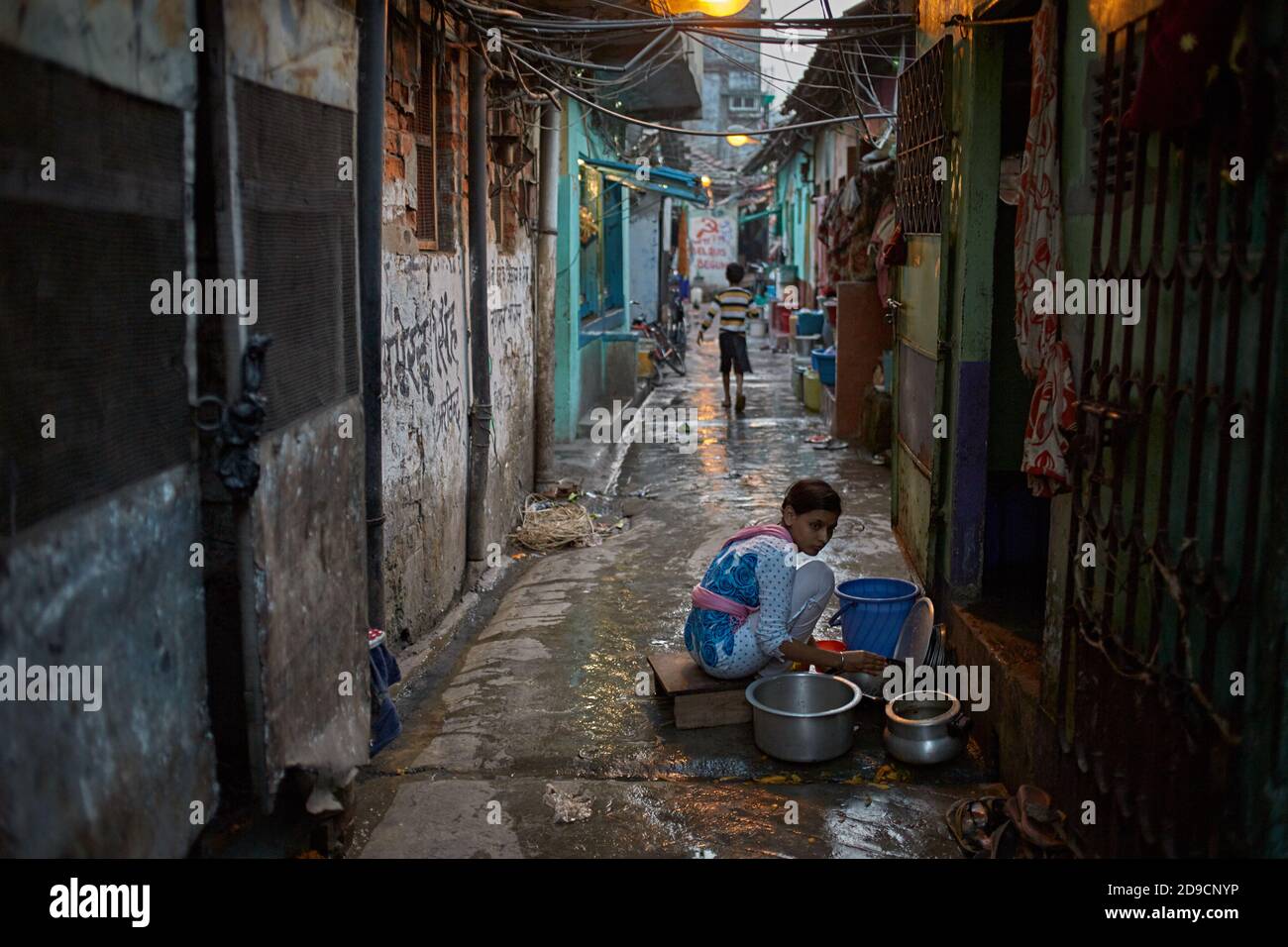 Kolkata, India, gennaio 2016. Una ragazza che lavora piatti di lavaggio nel mezzo di una strada stretta. Foto Stock