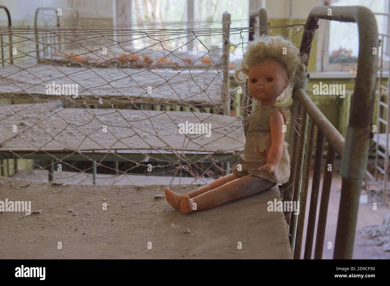 Una bambola sporca su un lettino per bambini arrugginito. Camera da letto abbandonata in asilo. Zona radioattiva di Chernobyl. Foto Stock