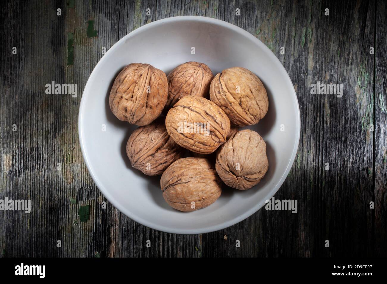 Foto dall'alto di un mazzo di noci secche in una Ciotola in ceramica su sfondo in legno decaduto Foto Stock