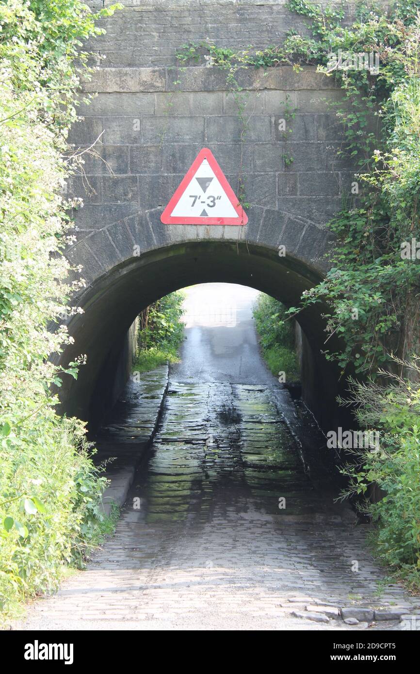 Ponte di canale in mattoni con strada acciottolata bagnata, e cartello di altezza sopra, a Newburgh Lancashire, Regno Unito con spazio per la copia Foto Stock