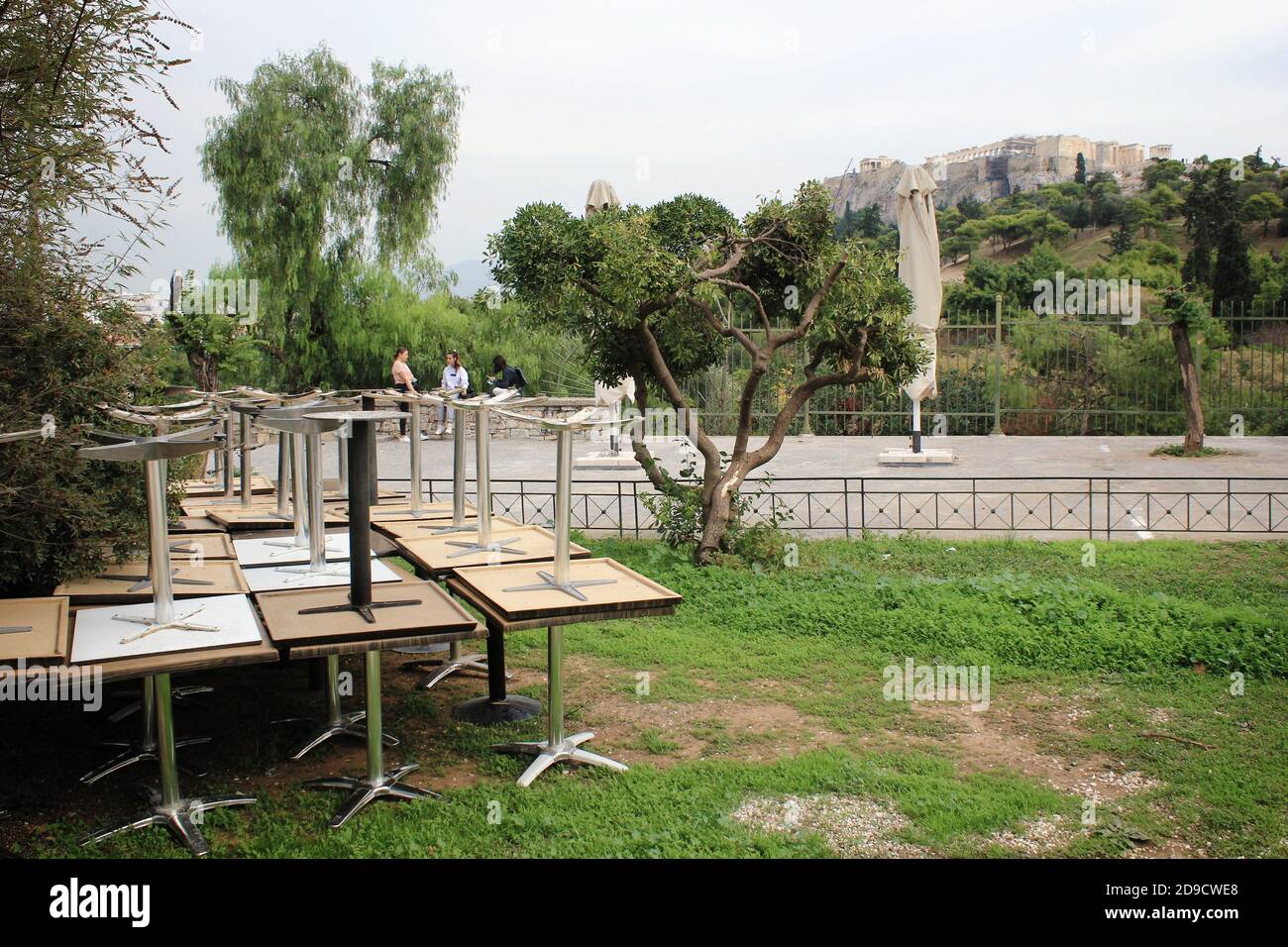 Grecia, Atene, 3 novembre 2020 - Tavoli accatastati all'esterno caffè-ristorante chiuso con la collina dell'Acropoli sullo sfondo, dopo l'annuncio di Covi Foto Stock