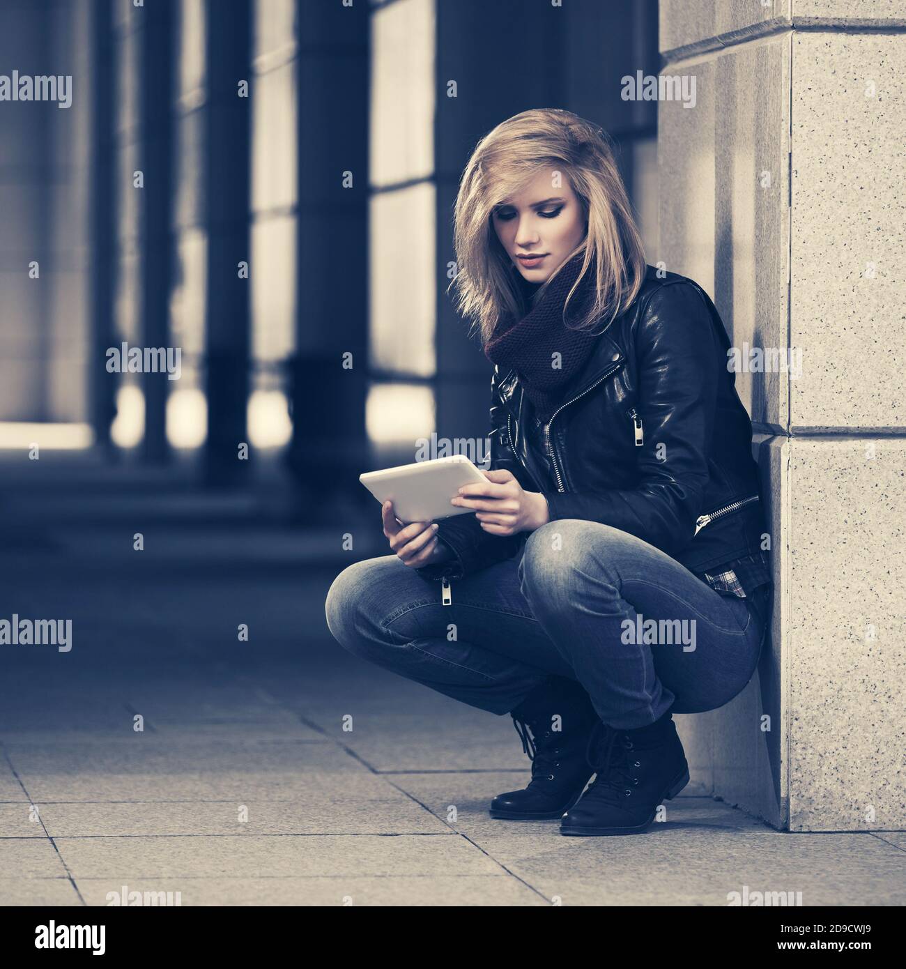Giovane donna alla moda che usa il tablet digitale in città elegante strada modello femminile con giacca in pelle nera e jeans blu scuro Foto Stock