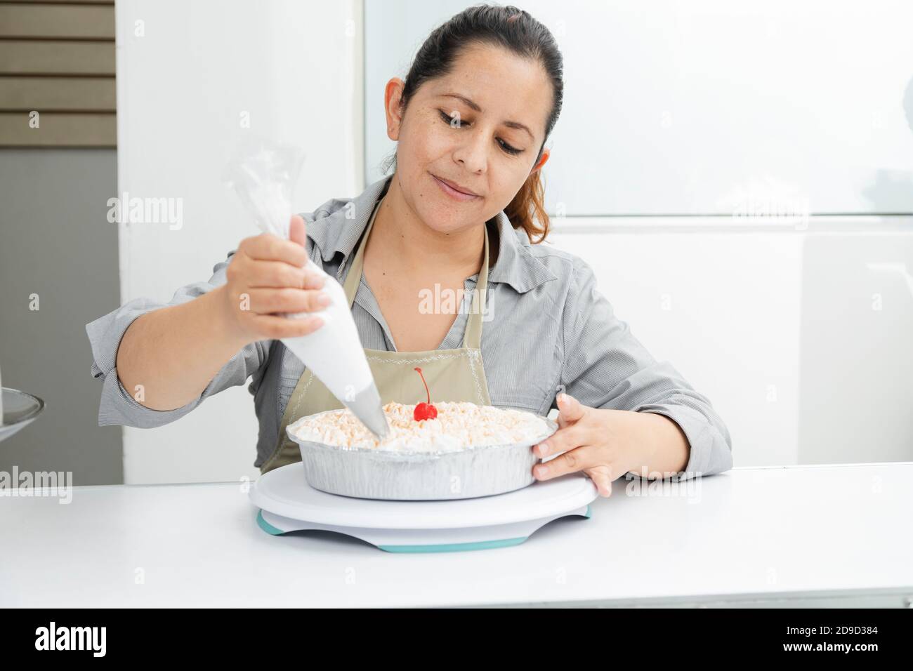 Donna ispanica nella sua pasticceria che decora una torta - donna mettere la panna montata sulla torta appena sfornata - donna intraprendente Foto Stock