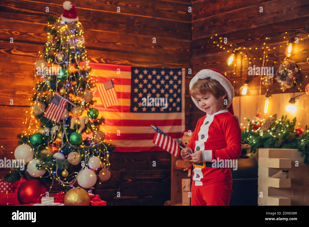 Concetto di tradizioni americane. Carino bambino festeggia il natale. Bandiera americana di umore allegro. Capretto gioca americano bandiera albero di natale Foto Stock