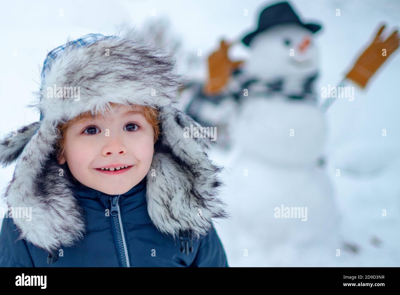 Pupazzo di neve e bambino divertente l'amico è in piedi in cappello  invernale e sciarpa con naso rosso. Fare pupazzo di neve e inverno  divertimento per i bambini. Ragazzo divertente che posa