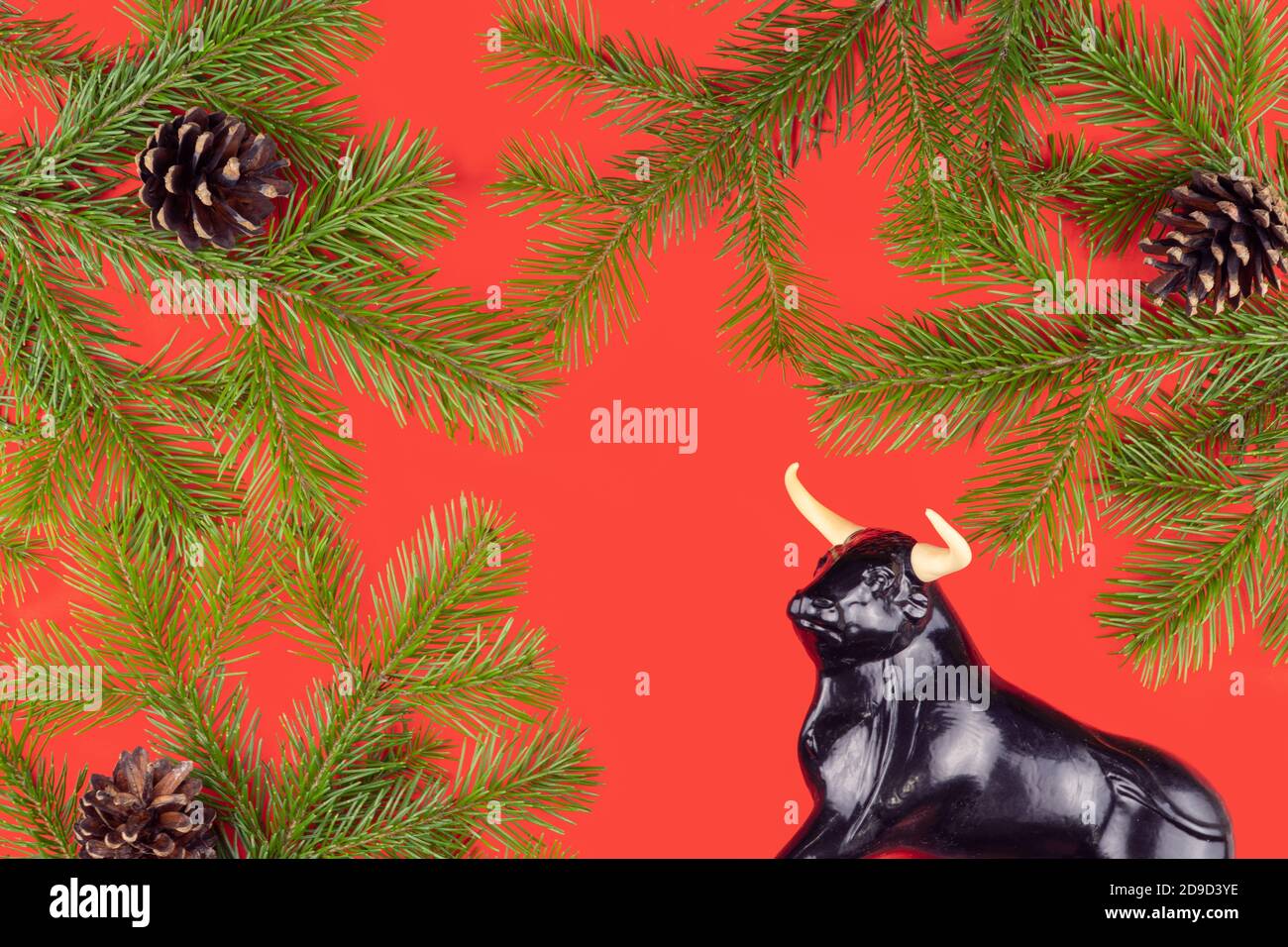 Statuetta di un toro su sfondo rosso di Natale. Fuoco selettivo. Decorazioni festive e rami di abete con coni. Festa di Capodanno. Foto Stock