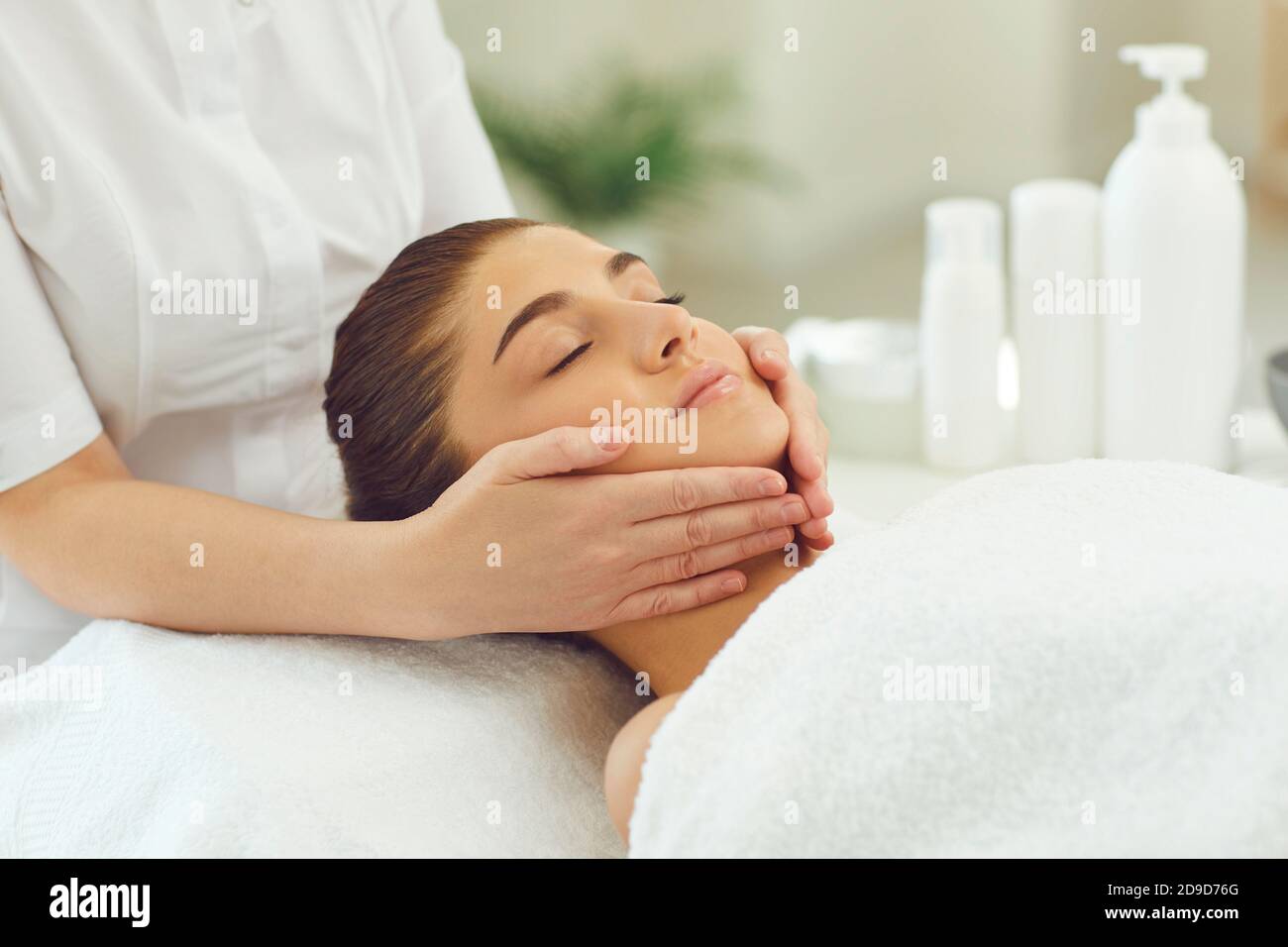 Donna che ottiene procedura di massaggio viso rilassante dalle mani di massaggiatore Foto Stock